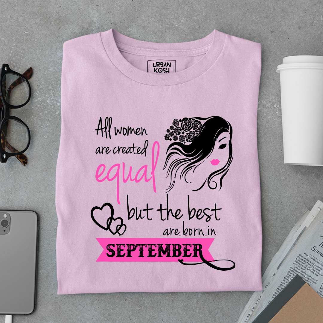 Pink t-shirt with text and graphic on a gray surface with accessories.