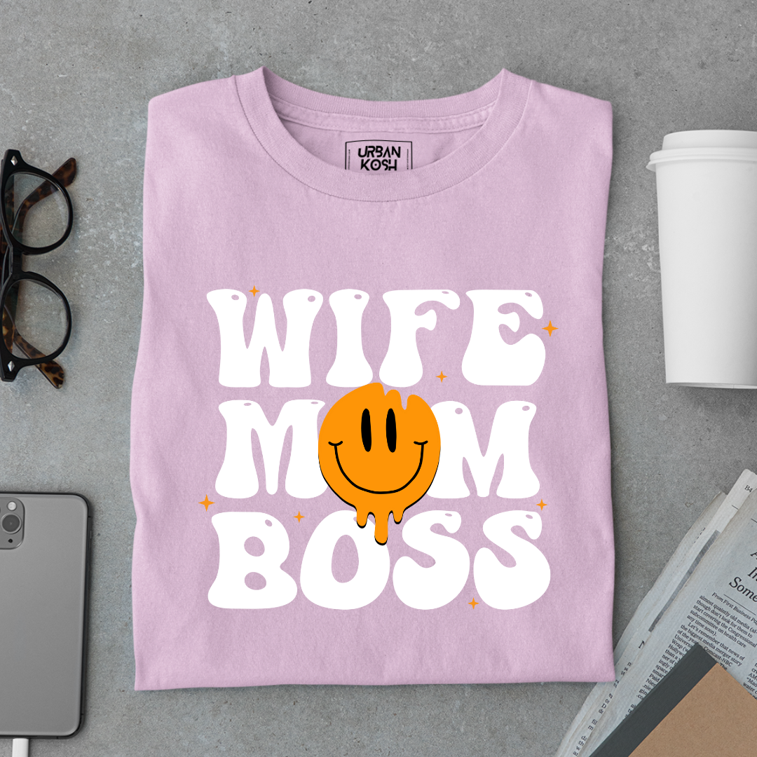 Purple t-shirt with 'WIFE MOM BOSS' text and smiley face on a gray surface with glasses and a cup.